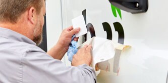 Mies teippaamassa kirjaimia autoon
