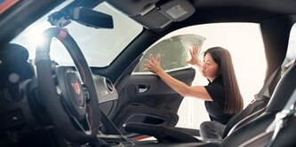 Nainen kiinnittämässä ikkunakalvoa autoon
