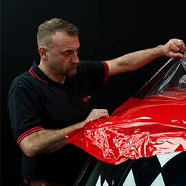 Mies asentamassa 3M Autoteippaus -teippiä auton etuosaan.