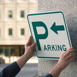 Henkilö, joka asentaa pysäköintikylttiä betoniseinään