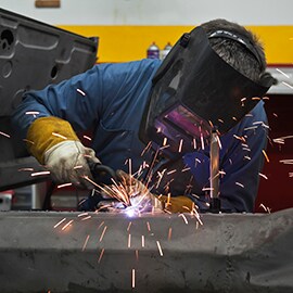 Kipinät sinkoilevat, kun teknikko hitsaa metallipintoja yhteen tehtaalla