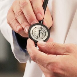 Lähikuva lääkäristä, joka pitää kädessään 3M Littmann -stetoskoopin rintakappaletta, jonka kalvolla on Littmann -sinetti.